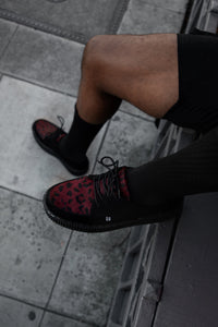 Person wearing black shoes with red patterns on a sidewalk